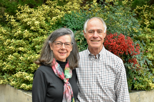 A man and woman smile in front of a green and red hedge
